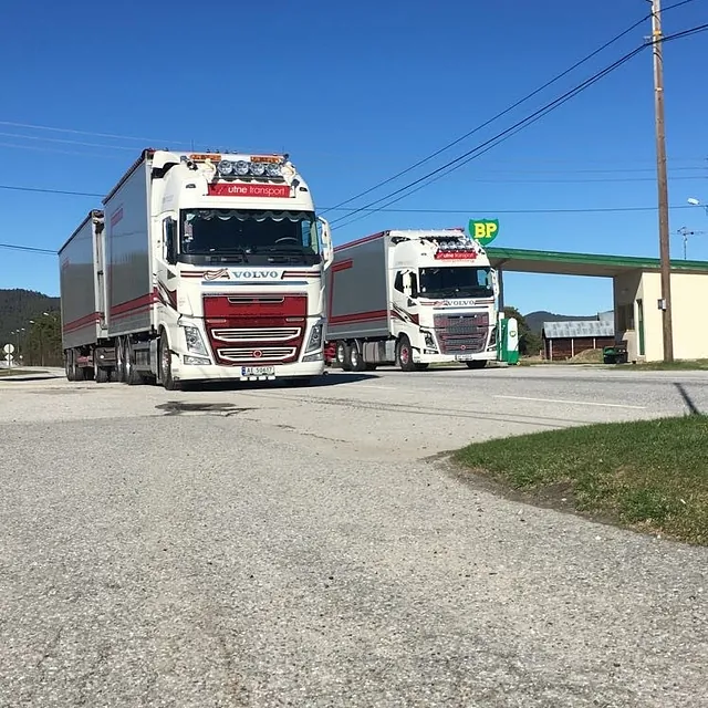To Volvo-trekkere med trailere foran en bensinstasjon.